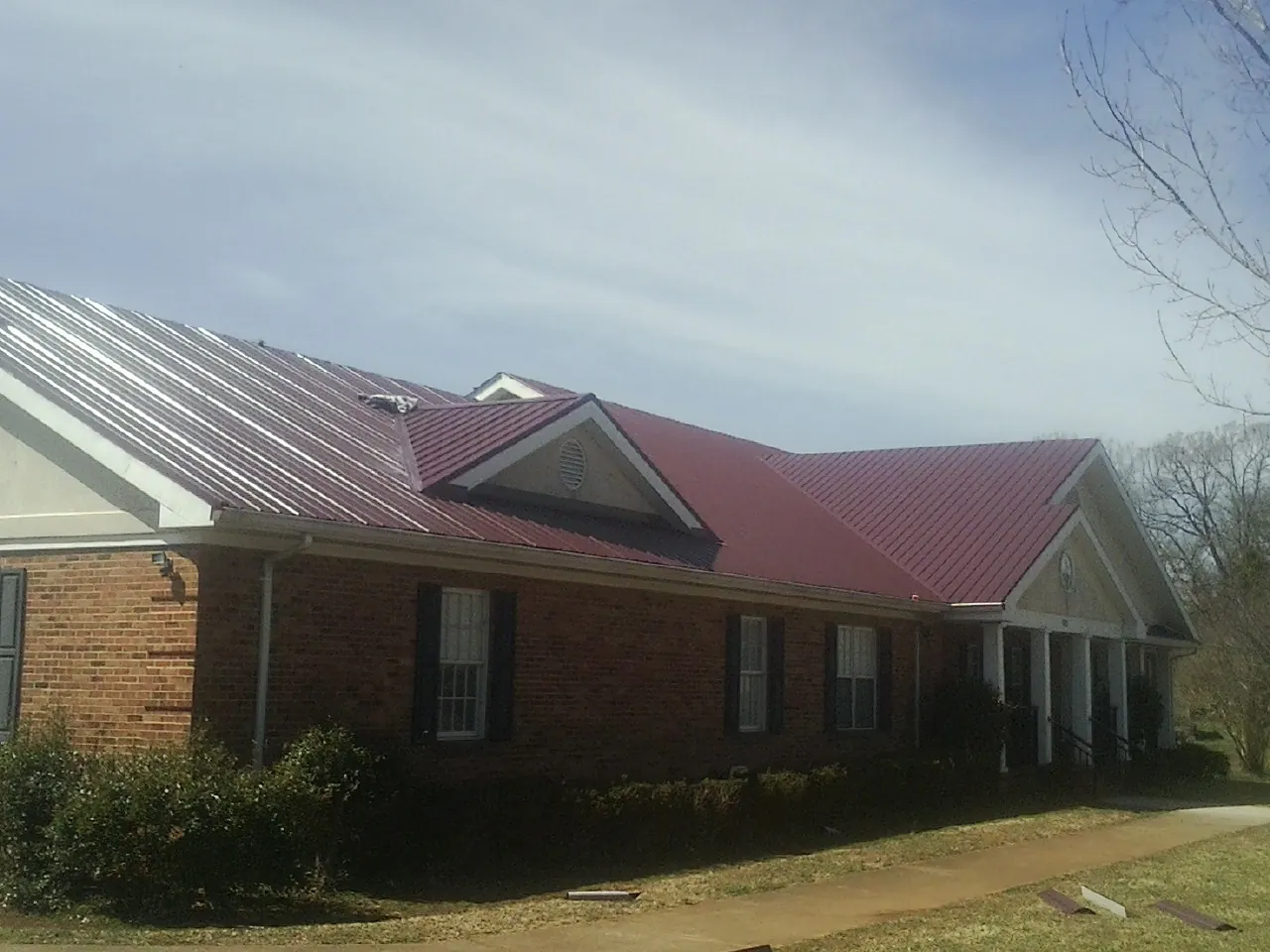 Red metal roof with gabled entries on a long brick building, from a Hail Damage Roof Repair job in Wallowa