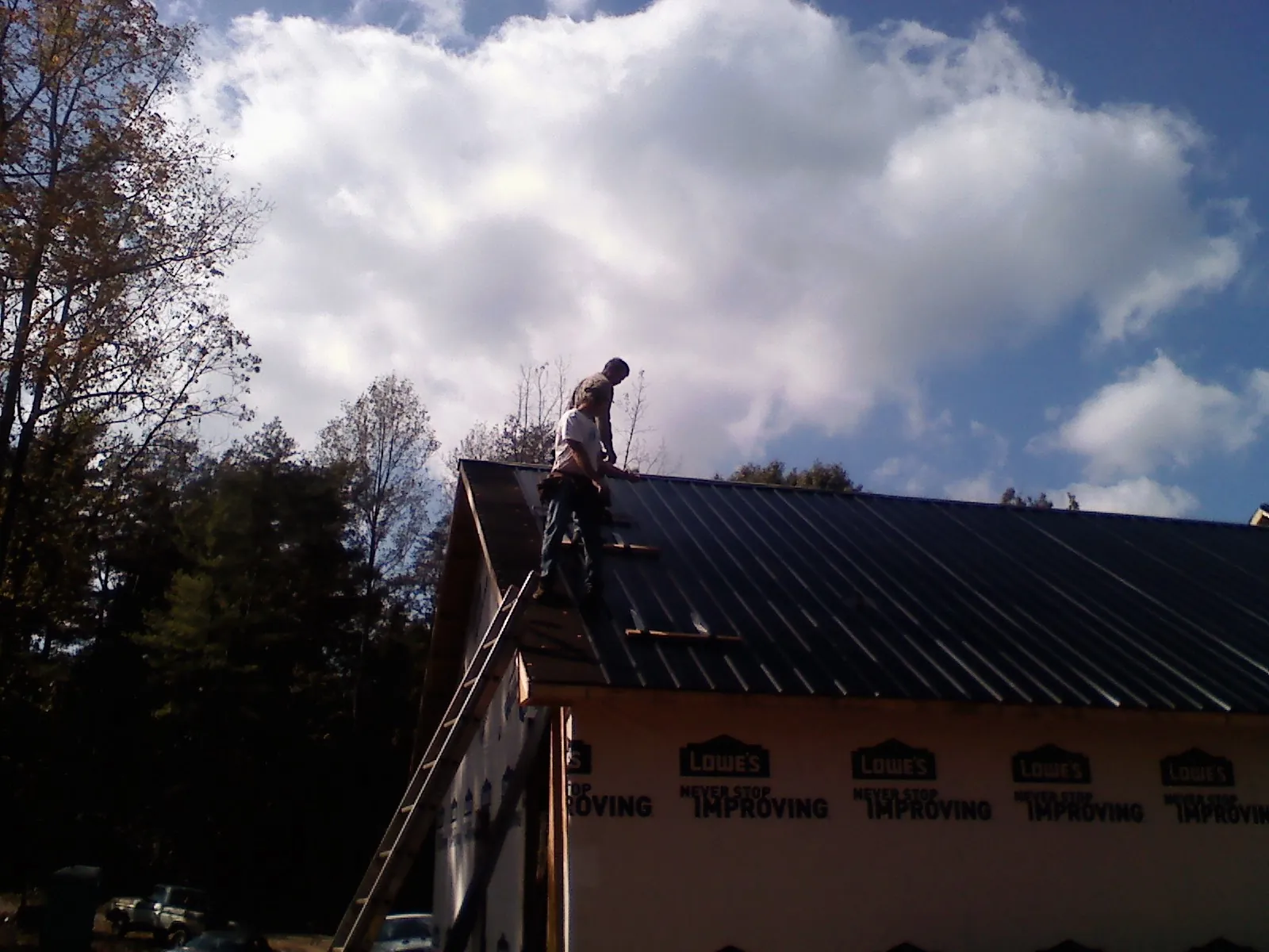 Roofer fastening dark metal panels high against a cloudy sky, from a Roof Inspection job in Wallowa