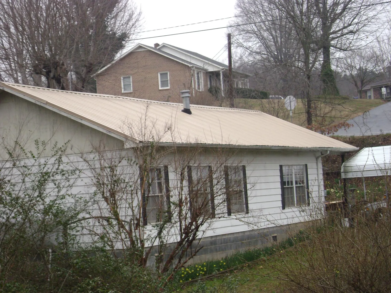 Tan metal roof on a white sided house set into a hillside — Commercial Roofing by Roofing Brothers in Wallowa